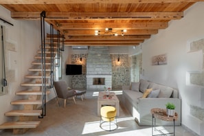 A modern interior with a wooden staircase, stone fireplace, and a cozy seating area. - Luxury Villa Dimitra with Private Swimming pool (Kato Vathia)