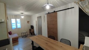 Ein Zimmer mit einem Holzesstisch, schwarzen Stühlen, einem Fernseher auf einem Holzboden und einer Schiebetür sowie einem Fenster mit Vorhängen.