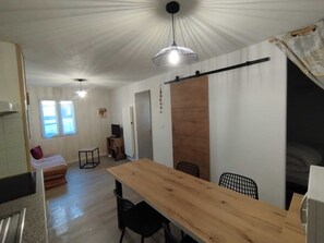 Quarto com uma mesa de jantar de madeira, cadeiras pretas, uma TV sobre um móvel de madeira, uma porta de correr e uma janela com cortinas.