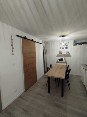 Uma cozinha compacta com mesa e cadeiras de madeira, luminária pendente e porta deslizante.