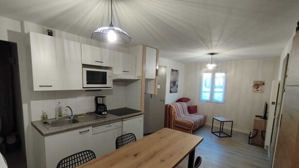 Eine kompakte Küche mit Mikrowelle, Spüle und Kaffeemaschine, ein Esstisch mit Stühlen, eine Couch und ein kleiner Tisch mit Lampe.