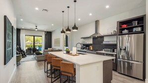 Et moderne køkken med en central ø, barstole, et rustfrit stål køleskab og et spiseområde med udsigt.