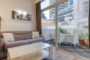 A modern living room with a sofa, a glass coffee table, and a view of a balcony with outdoor furniture. - St. Julian's Studio 404 - Near Beach & Paceville (Saint Julian's)