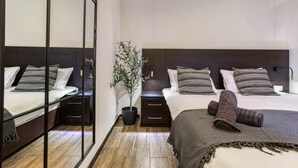 Moderni hotellihuone, jossa on suuri peili, raidallinen vuodevaatteilla varustettu sänky, yöpöytä, ruukussa oleva kasvi ja tumma puinen pääty.