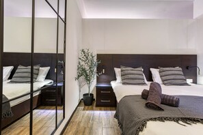 A modern hotel room with a large mirror, a bed with striped bedding, a nightstand, a potted plant, and a dark wooden headboard. - St. Julian's Studio 404 - Near Beach & Paceville (Saint Julian's)