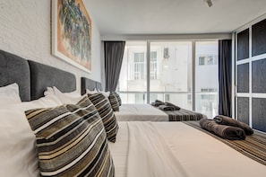 A hotel room with a large window, a bed with striped bedding, a grey headboard, and a painting on the wall. - St. Julian's Apartment 501 - Near Beach &Paceville (Saint Julian's)
