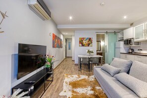 Ein modernes Wohnzimmer mit Fernseher, einer Couch, einem Essbereich und einer Küche.
