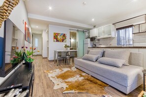 Ein modernes Wohnzimmer mit Sofa, Fernseher, Essbereich und Küche.