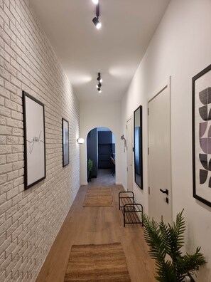 Ein Flur mit weißen Ziegelwänden, gerahmten Kunstwerken, Holzboden und einer Tür zu einem Zimmer.