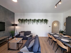 Ein modernes Wohnzimmer mit Sofa, Couchtisch und Essbereich mit Stühlen und einem Tisch für vier Personen.