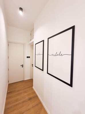 Ein Flur mit zwei gerahmten Kunstwerken an der Wand, einer weißen Tür und Holzböden.
