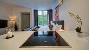 Et moderne hotelværelse med seng, fladskærms-tv, indbygget komfur og udsigt til grønne områder.