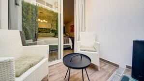 En balkon med fletmøbler, en glasdør der fører til en have, og et sort bord.