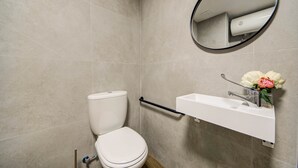 Et badeværelse med toilet, håndvask, spejl og et håndklædestativ.