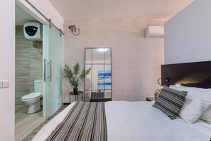 Et moderne hotelværelse med en seng, et sengebord, en potteplante, et spejl og havudsigt.