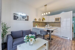 Eine moderne Küche mit weißen Schränken, einer Mikrowelle und einem Essbereich mit grauem Sofa und weißem Tisch.