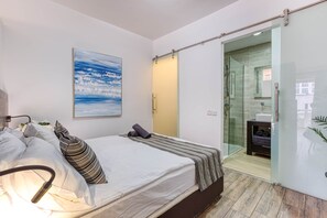 A modern bedroom with a bed, a bedside lamp, a glass shower enclosure, and a bathroom visible through a sliding door. - St. Julian's Studio 401 - Near Beach & Paceville (Saint Julian's)