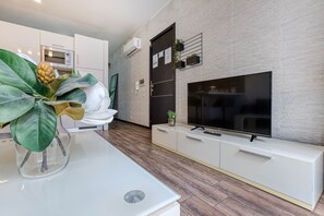 Eine moderne Küche mit Einbauofen, weißen Schränken, einer weißen Arbeitsplatte und einem großen Fernseher auf einem weißen Schrank.