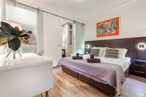 Ein modernes Schlafzimmer mit Bett, Nachttischen, einer Dusche mit Glastrennwand und einem großen abstrakten Gemälde.