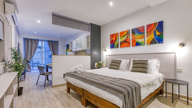 Um quarto moderno com cama de madeira, uma escrivaninha e uma cadeira, vista para o exterior e obras de arte coloridas nas paredes.