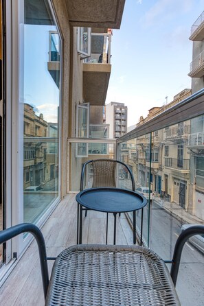 A balcony with wicker chairs, a small table, and a view of the cityscape through large windows. - St. Julian's Studio 201 - Near Beach & Paceville (Saint Julian's)