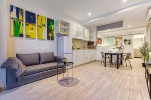 A modern living room with a sofa, a small round table, and a dining area with chairs. There is a kitchen area with cabinets and a microwave. - St. Julian's Studio 201 - Near Beach & Paceville (Saint Julian's)