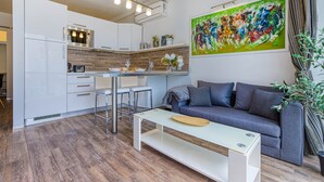 A modern kitchen with white cabinets, a dining area with a white table and bar stools, a gray sofa, and a large abstract painting on the wall. - St. Julian's Studio 302 - Near Beach & Paceville (Saint Julian's)
