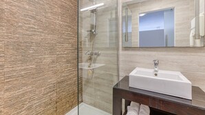 A modern bathroom with a glass shower enclosure, a white sink, and a wooden vanity. - St. Julian's Studio 302 - Near Beach & Paceville (Saint Julian's)