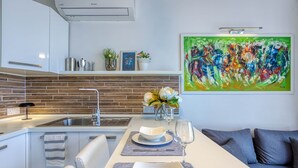 A modern kitchen with a brick backsplash, white cabinetry, and a dining area with a white table and blue placemats. - St. Julian's Studio 302 - Near Beach & Paceville (Saint Julian's)
