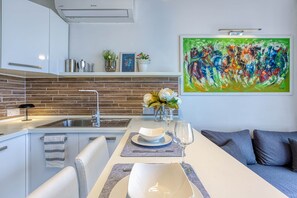 Eine moderne Küche mit Ziegelrückwand, weißen Schränken und einem Essbereich mit weißem Tisch und blauen Untersetzern.