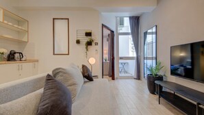 A modern living room with a sofa, TV, and a dining area visible through an open door. - St. Julian's Studio 204 - Near Beach & Paceville (Saint Julian's)