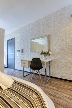 Ein Hotelzimmer mit einem Bett, einem Schreibtisch mit Stuhl, einem Spiegel und einer Vase mit Blumen.