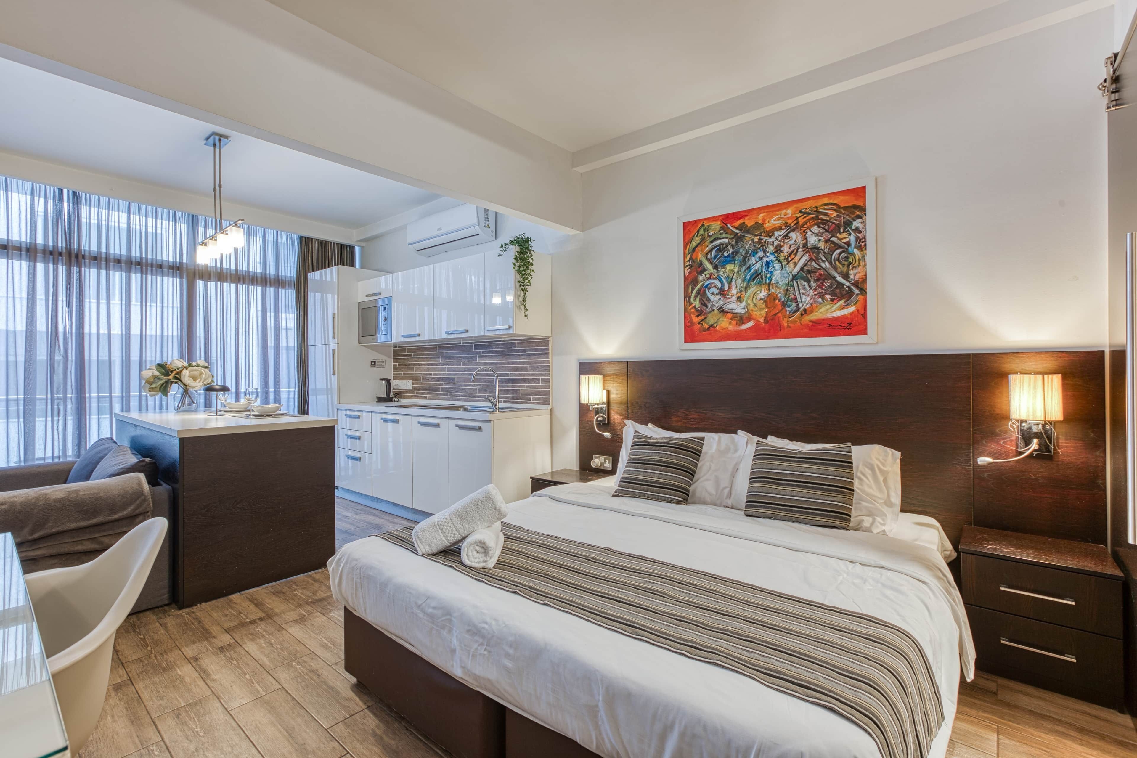 Ein modernes Hotelzimmer mit einem großen Bett, einem Schreibtisch, einer Küchenzeile und einem Essbereich.