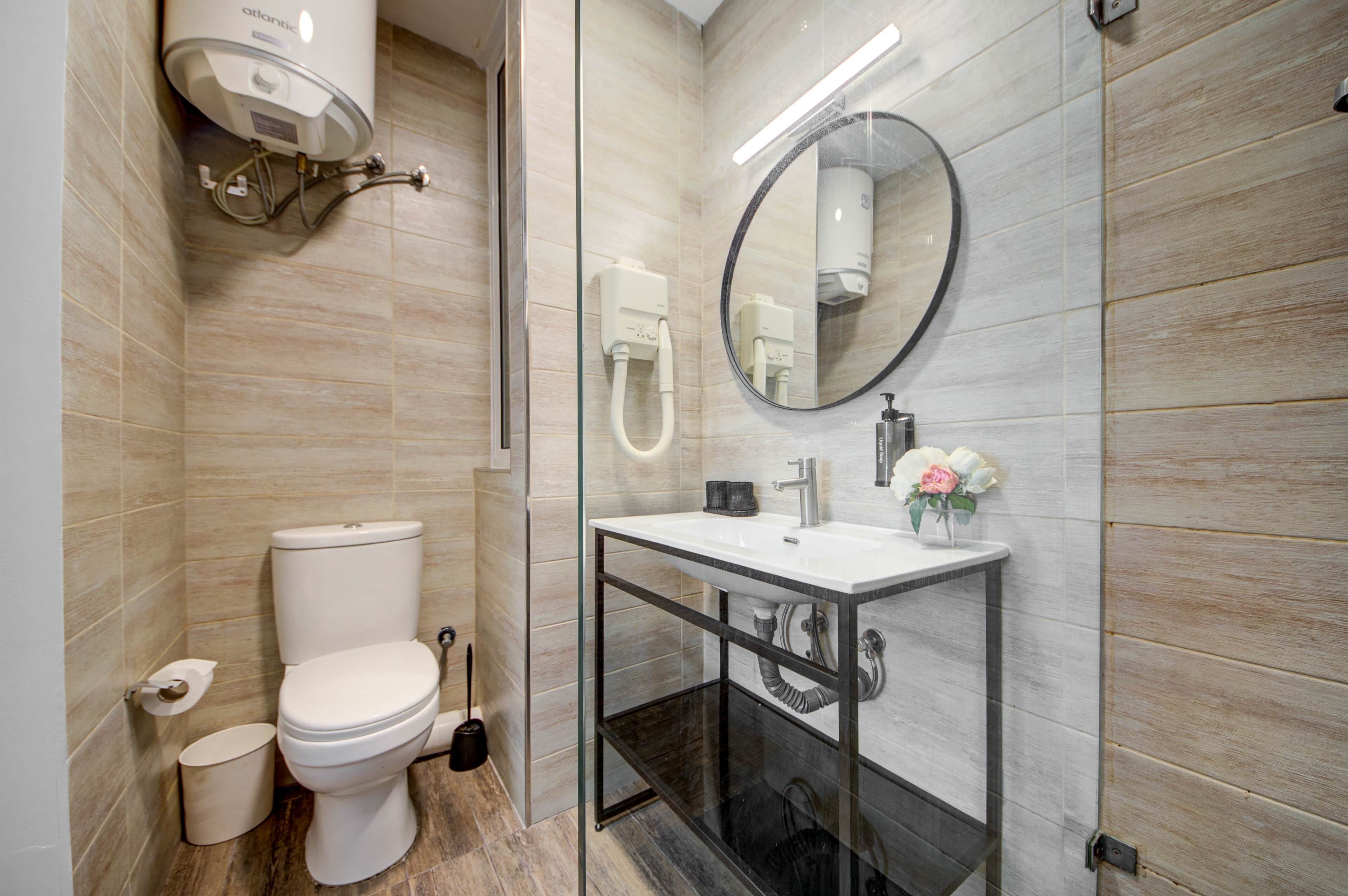A modern bathroom with a toilet, a glass-enclosed sink, a mirror, and a handheld showerhead.
