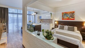 Moderni hotellihuone, jossa on sänky, yöpöytä ja näkymä keittiöön ja olohuoneeseen.