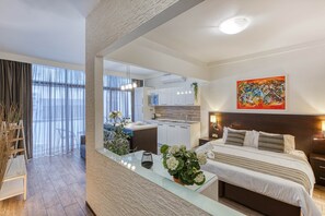 Ein modernes Hotelzimmer mit Bett, Nachttisch und Blick auf die Küche sowie den Wohnbereich.