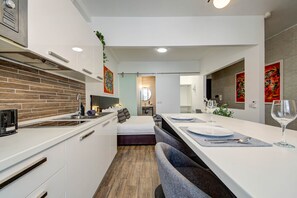 A modern kitchen with a brick backsplash, a dining area with a long table, and a bedroom with a bed and nightstand. - St. Julian's Studio 203 - Near Beach & Paceville (Saint Julian's)