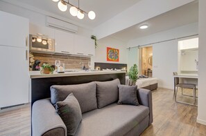 Eine moderne Küche mit integriertem Mikrowellenherd, ein Essbereich mit Glastisch und ein Wohnzimmer mit Sofa.