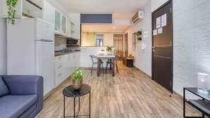 A compact kitchen with white cabinets, a microwave, and a refrigerator. There is a dining area with a table and chairs, and a sofa in the foreground. - St. Julian's Studio 301 - Near Beach & Paceville (Saint Julian's)