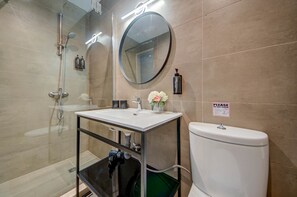 Ein modernes Badezimmer mit Duschkabine aus Glas, einem runden Spiegel, einem weißen Waschbecken und einer Toilette.