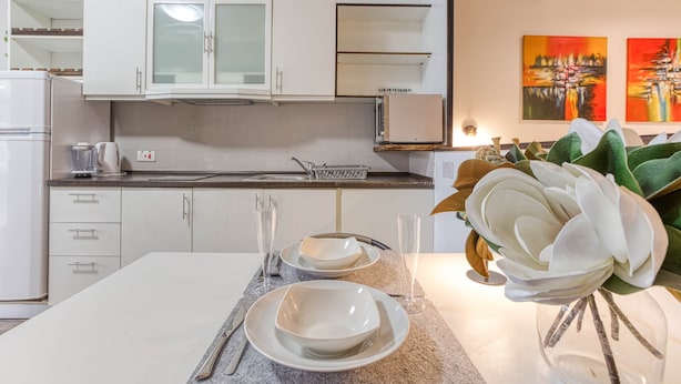 A modern kitchen with white cabinets, a granite countertop, and a dining area with a white table set for two. - St. Julian's Studio 301 - Near Beach & Paceville (Saint Julian's)