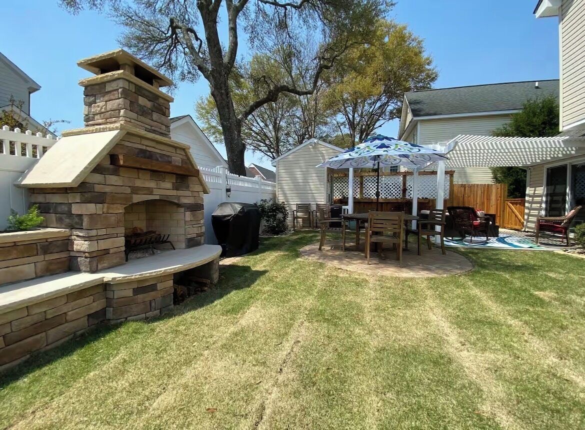 Een achtertuin met een stenen barbecue, een overdekte patio tafel en een houten terras.
