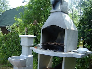 Un horno de piedra al aire libre con chimenea, rodeado de vegetación.