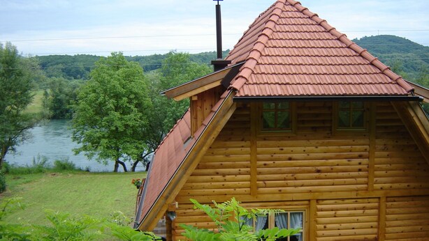 A wooden cabin with a sloped roof, a window, and a view of a river and forest. - In quiet Vrhpolje, cozy house with 3 bedrooms. With the best view in the region. (Vrhpolje)