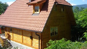 A wooden cabin with a sloped roof, a chimney, and a small porch. - In quiet Vrhpolje, cozy house with 3 bedrooms. With the best view in the region. (Vrhpolje)