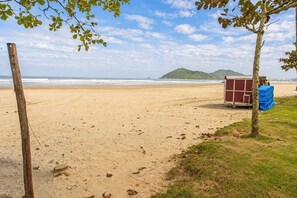 A beach with a wooden post, a small structure, and a tree. - Apto com Piscina e Vaga a 750m da Praia da Enseada (Bertioga)