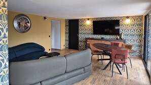 En moderne stue med en sofa, et spisebord med stole og et fladskærms-tv monteret på væggen.