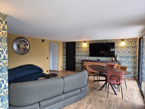 Ein modernes Wohnzimmer mit einer Couch, einem Esstisch mit Stühlen und einem an der Wand montierten Flachbildfernseher.