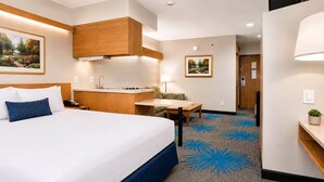 A hotel room with a bed, a desk, a chair, a sink, and a small table.