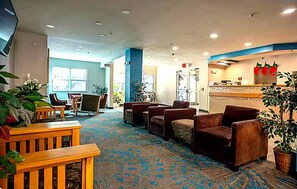 A hotel lobby with seating areas, a reception desk, and large windows.